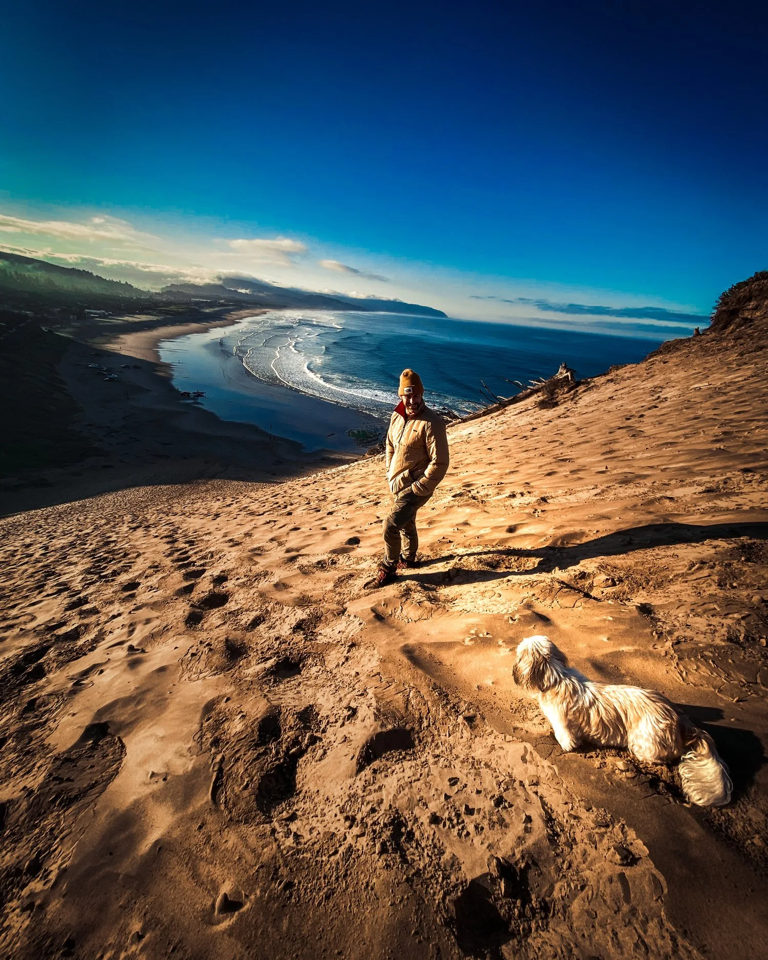 JK and Piper on an Oregon coast dune at golden hour, the Pacific curving out behind them